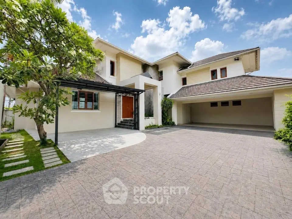 Luxurious modern house with spacious driveway and lush greenery under a clear blue sky.