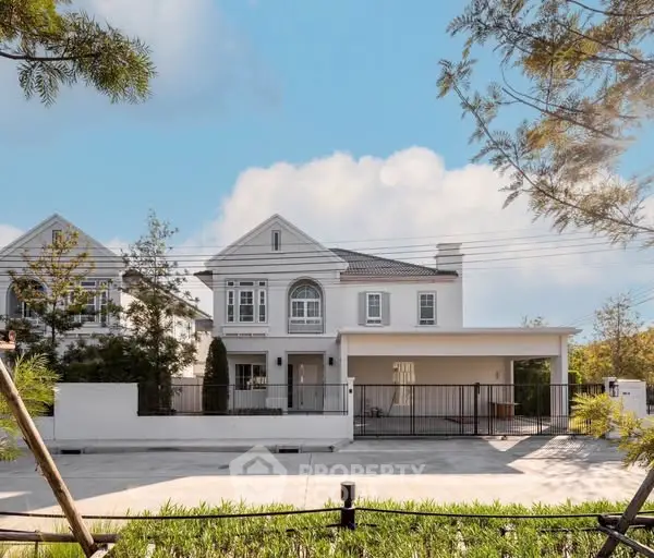 Elegant white house with spacious driveway and lush greenery under a clear blue sky.