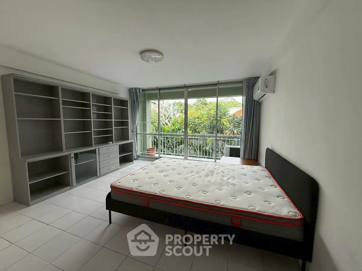 Spacious bedroom with large windows and garden view, featuring built-in shelves and air conditioning.