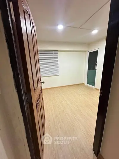 Spacious empty room with wooden flooring and sliding glass door, perfect for customization.