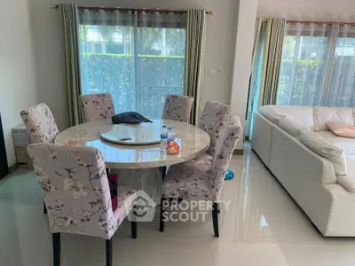 Elegant dining area with floral chairs and round table in a bright living room with large windows.