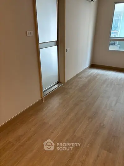 Spacious room with wooden flooring and large window, perfect for natural light.