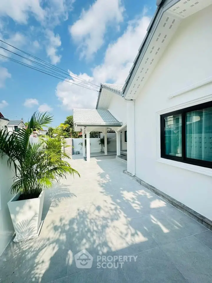 Charming white exterior house with spacious patio and lush greenery under a clear blue sky.