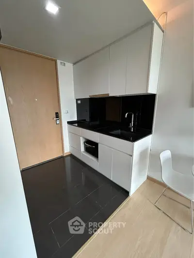 Modern compact kitchen with sleek black countertops and built-in appliances in a stylish apartment.