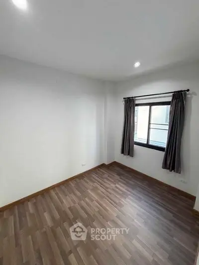 Spacious empty room with wooden flooring and window, perfect for customization.