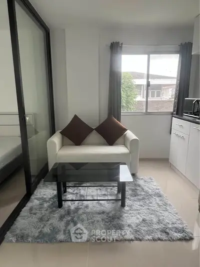 Modern living room with cozy sofa, glass coffee table, and plush rug in a bright apartment.