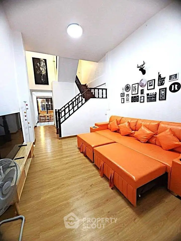 Spacious living room with vibrant orange sofa and stylish decor, perfect for modern living.