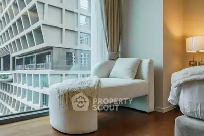 Modern bedroom with cozy seating and large window offering stunning urban view.