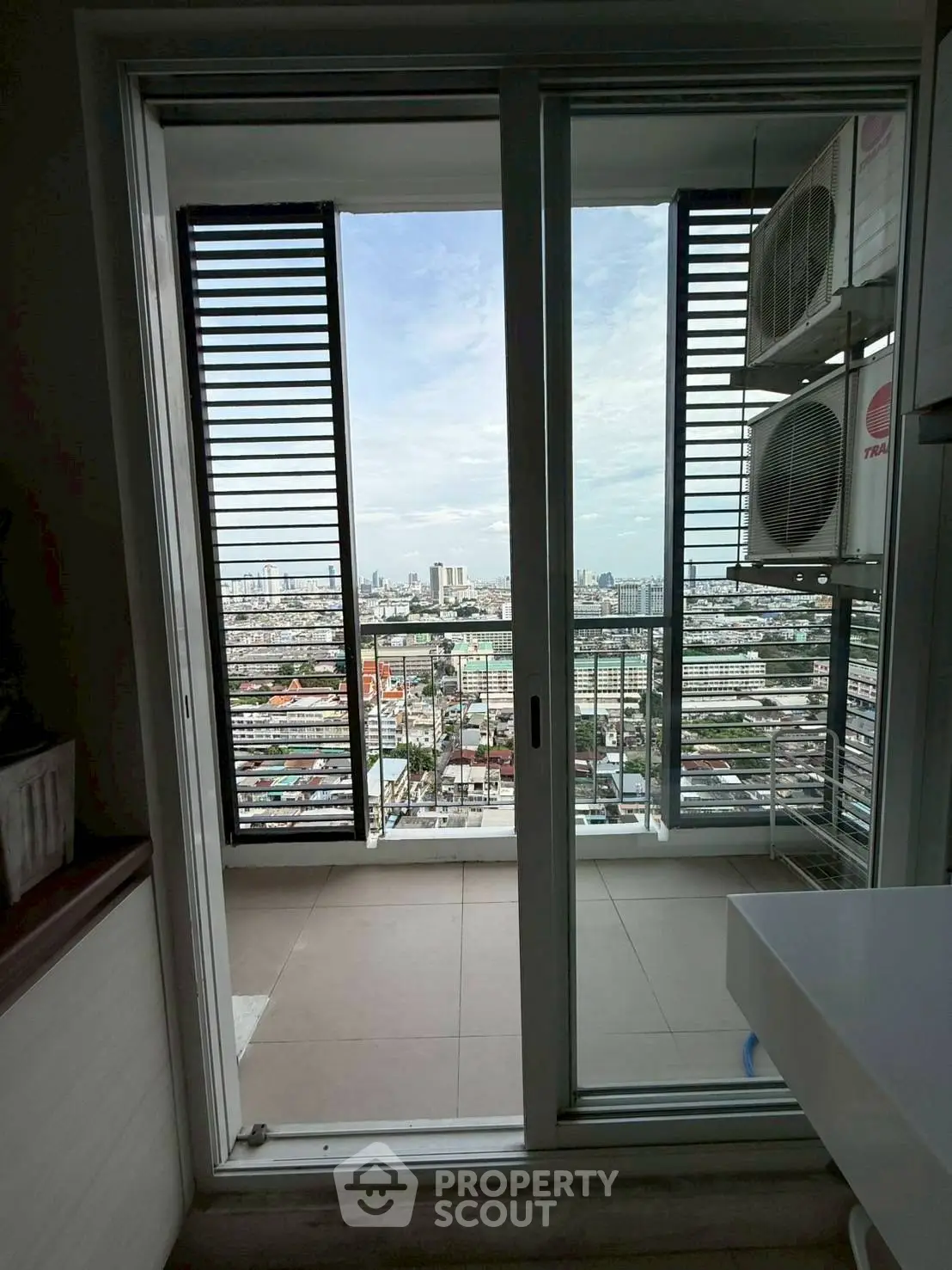 Stunning city view from modern balcony with sliding glass doors and air conditioning units.