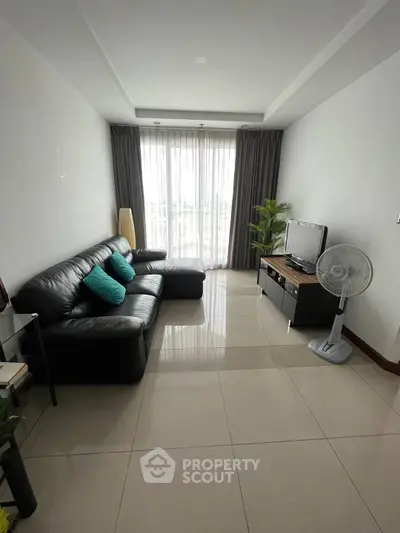 Modern living room with sleek black leather sofa and large window for natural light.