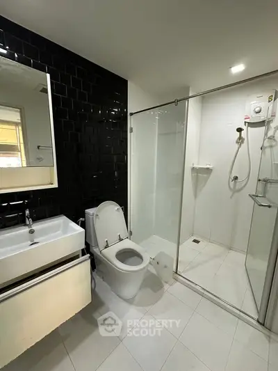 Modern bathroom with sleek black tile accent wall and glass shower enclosure.