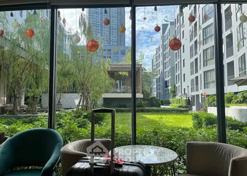 Modern apartment complex with lush garden view from lobby area, featuring stylish seating and large windows.