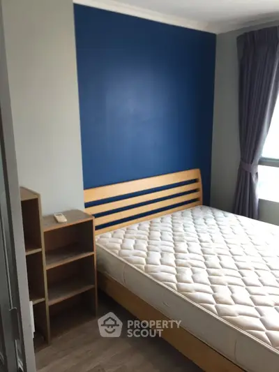 Modern bedroom with wooden bed frame and blue accent wall, natural light through window.