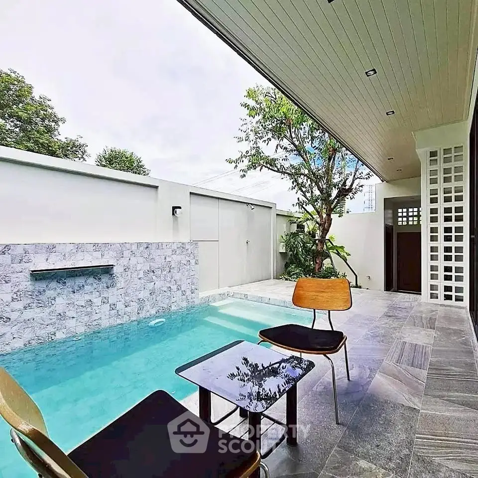 Modern outdoor pool area with stylish seating and elegant stone wall feature.