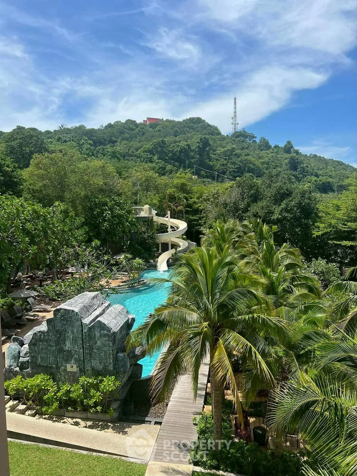 Luxurious resort pool with water slide and lush greenery, perfect for relaxation and leisure.