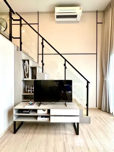 Modern living room with stylish staircase and TV unit, featuring sleek design and natural light.