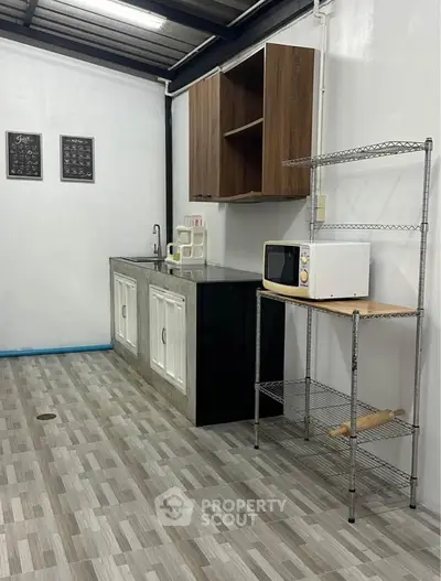 Modern kitchen with sleek cabinets and microwave on metal shelving, featuring stylish tiled flooring.