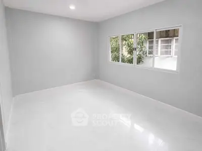 Spacious empty room with large window and white flooring, perfect for customization.