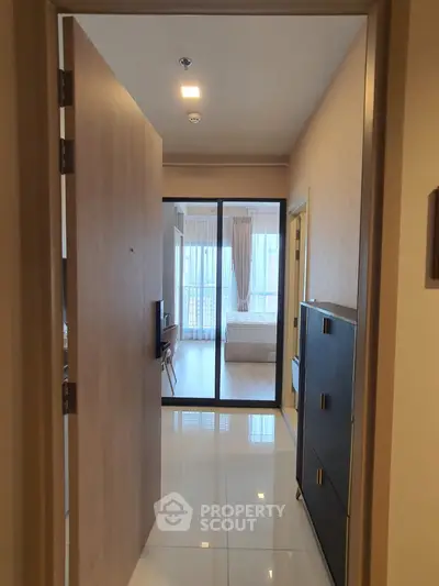 Modern apartment entrance leading to a bright bedroom with large windows and sleek flooring.
