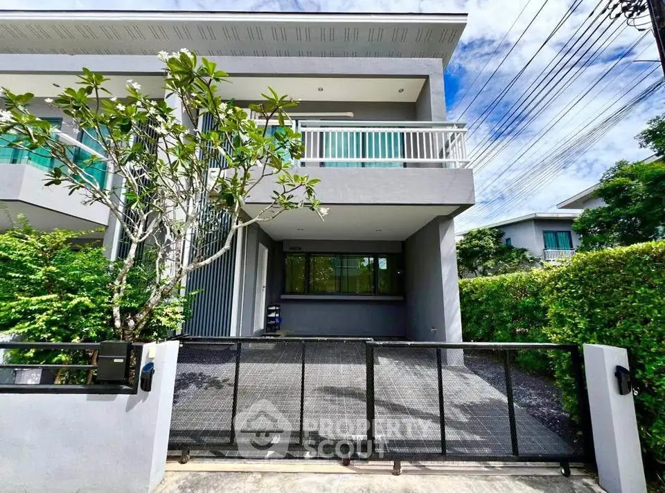 Modern two-story house with balcony and lush greenery, perfect for family living.