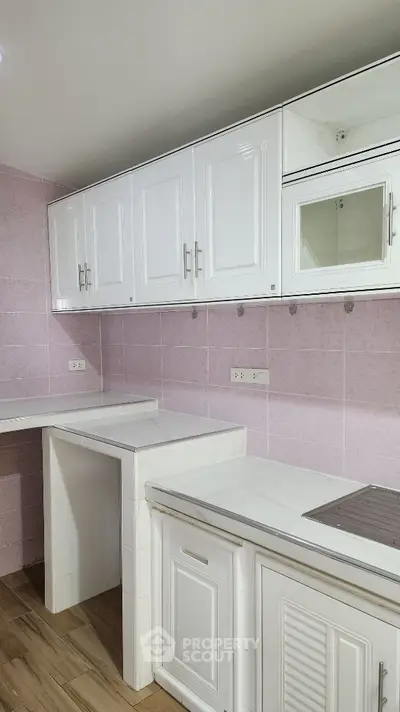 Modern kitchen with white cabinets and pink tiled walls, featuring a sleek design and ample storage space.