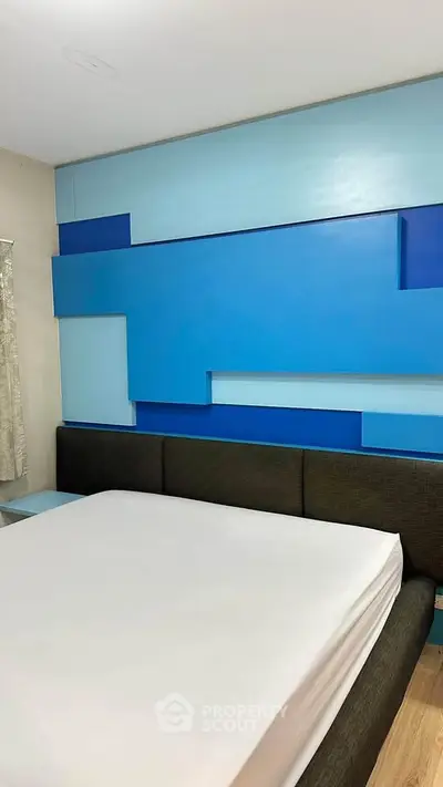 Modern bedroom with unique blue geometric wall design and sleek bed frame.