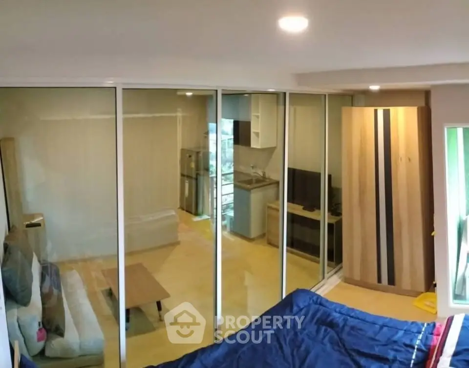 Modern studio apartment with glass partition, cozy living area, and compact kitchen.