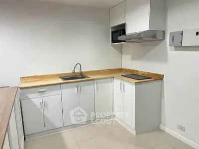 Modern kitchen with sleek white cabinets and wooden countertops, featuring a minimalist design.