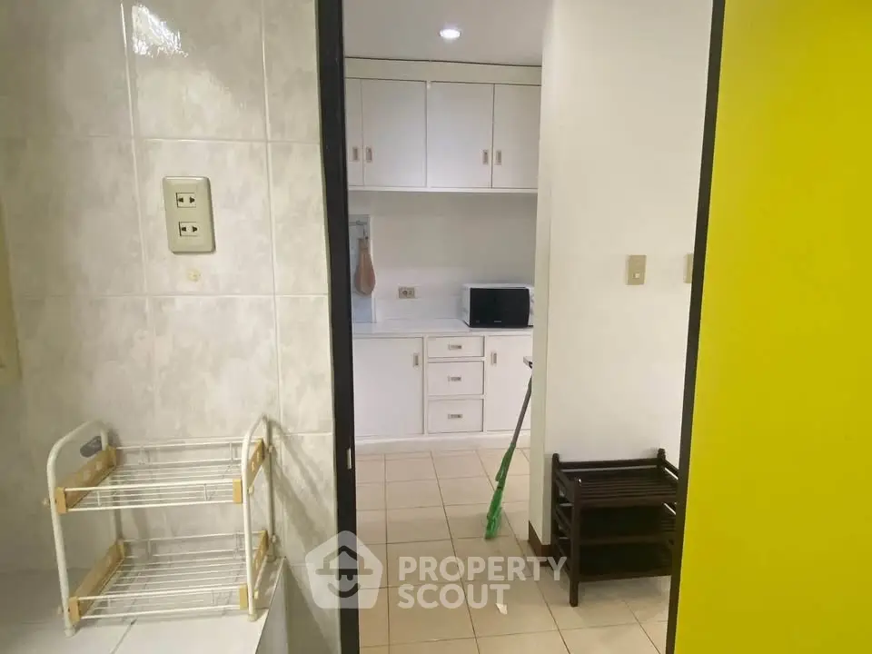 Cozy kitchen with white cabinets and microwave, featuring a tiled floor and bright yellow door.