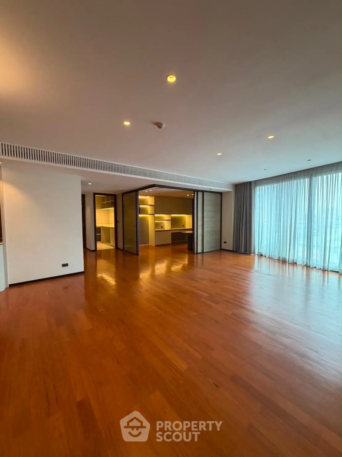 Spacious modern living room with wooden flooring and large windows for natural light.
