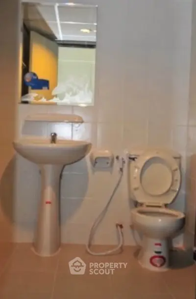 Modern bathroom with pedestal sink and toilet in a tiled setting.