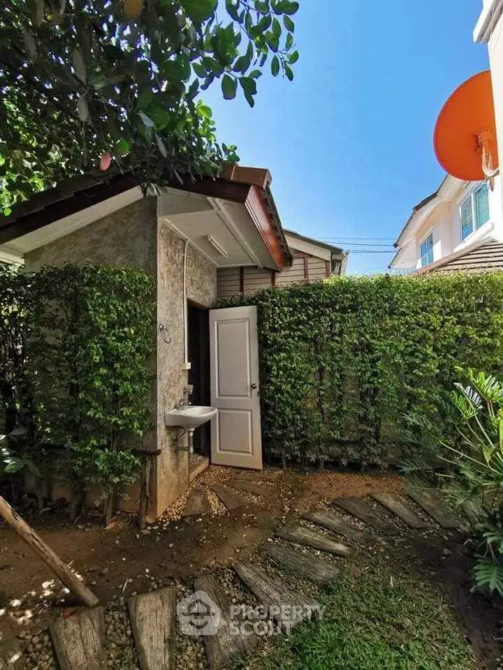 Charming garden pathway leading to a quaint outdoor shed with lush greenery and bright blue sky.