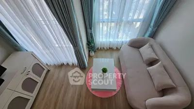 Modern living room with stylish sofa, coffee table, and large windows with curtains.