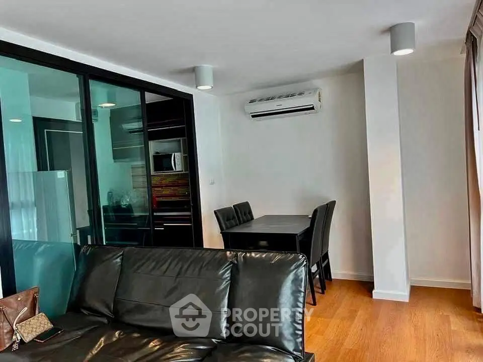 Modern living room with sleek black leather sofa and dining area in open layout apartment.