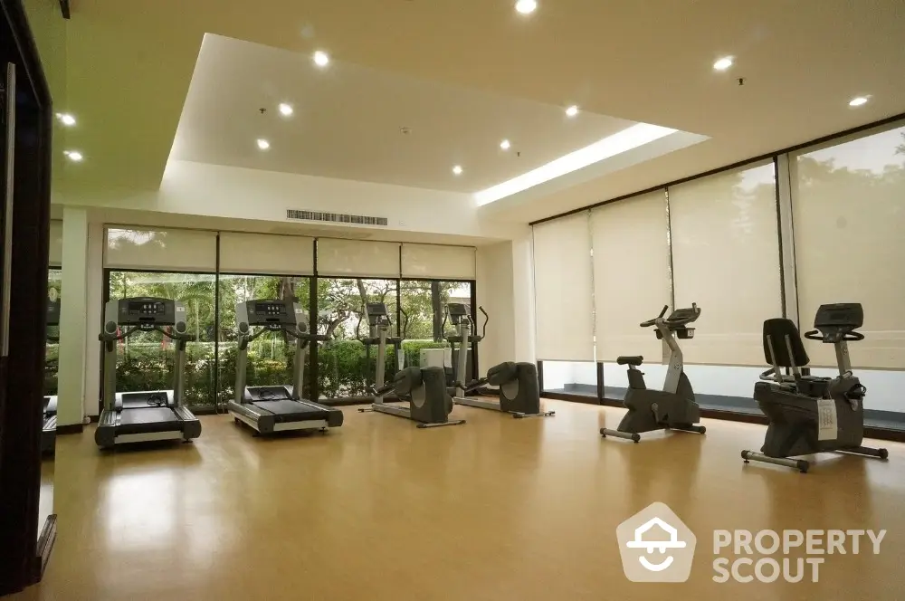 Spacious gym with modern equipment and large windows overlooking greenery.