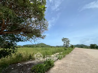 Scenic view of open land with lush greenery and distant hills under a clear blue sky, ideal for development.