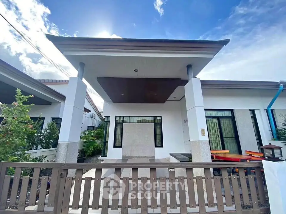 Modern single-story house with a stylish facade and fenced front yard under a clear blue sky.