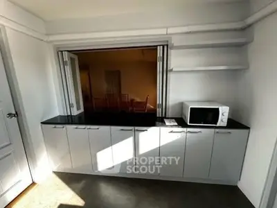 Modern kitchen with sleek cabinets and microwave, featuring open layout and ample storage.