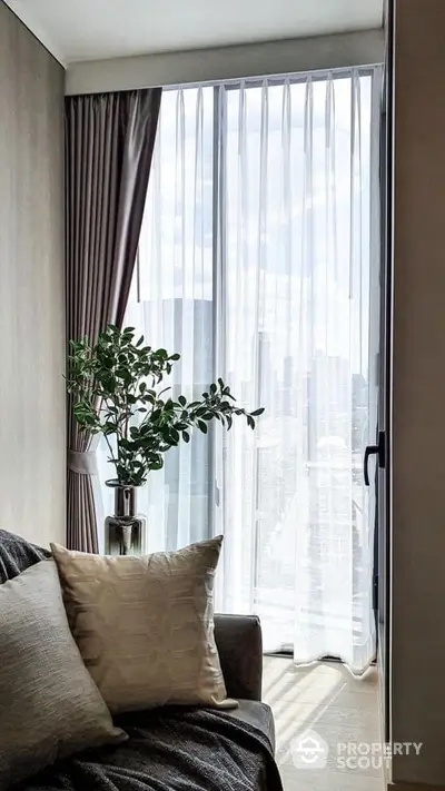 Stylish living room with large window and city view, featuring elegant curtains and cozy sofa.