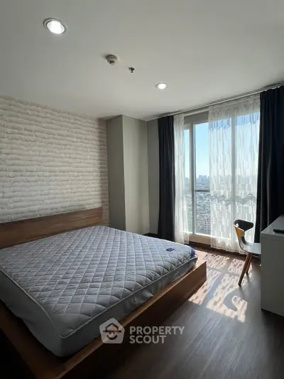 Modern bedroom with large window offering city view, featuring stylish furniture and ample natural light.