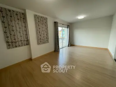 Spacious empty room with wooden flooring and large window for natural light.