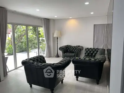 Elegant living room with classic leather sofas and large windows overlooking lush greenery.