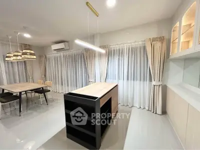Modern open-plan kitchen with sleek island and dining area, featuring elegant lighting and large windows.