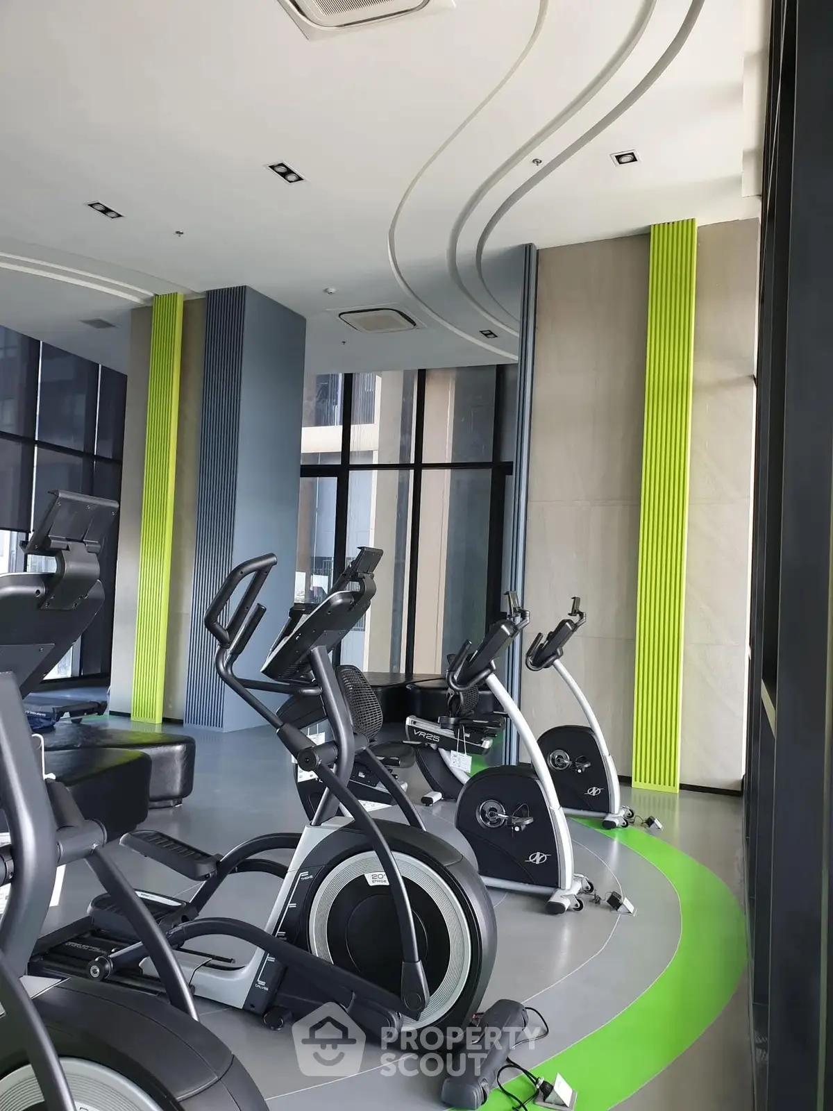 Modern gym with sleek exercise equipment and vibrant green accents in luxury building.
