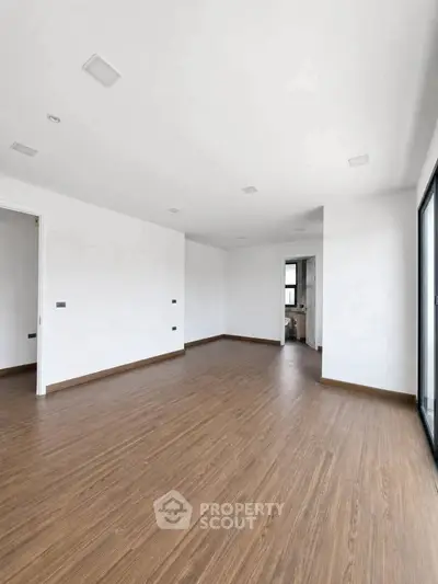 Spacious empty room with wooden flooring and large windows, perfect for customization.