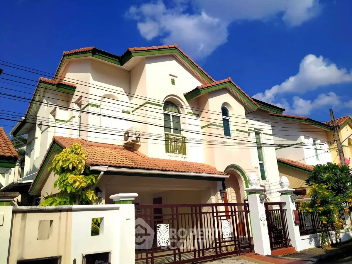 Elegant two-story house with red-tiled roof and gated entrance under a clear blue sky.