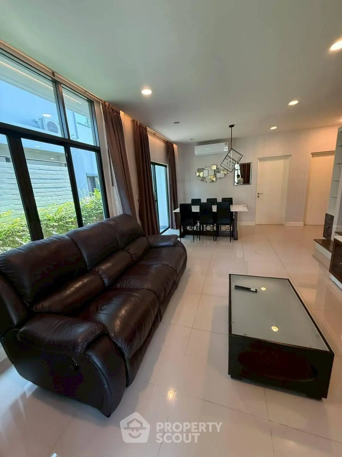 Spacious modern living room with leather sofa and dining area, large windows for natural light.