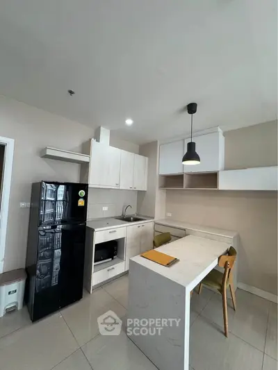 Modern kitchen with sleek design, featuring a black fridge, built-in oven, and stylish pendant lighting.