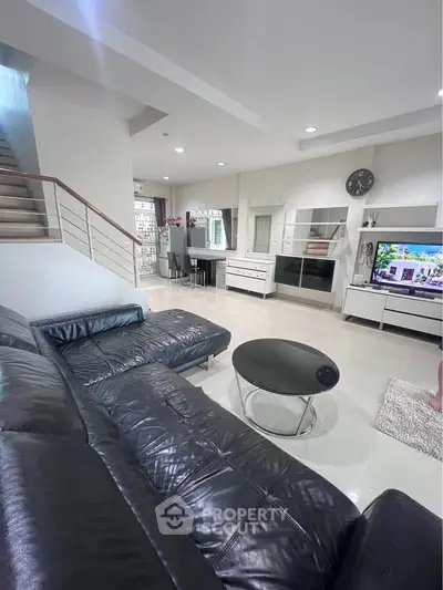 Spacious modern living room with sleek black leather sofa and open layout, perfect for entertaining.