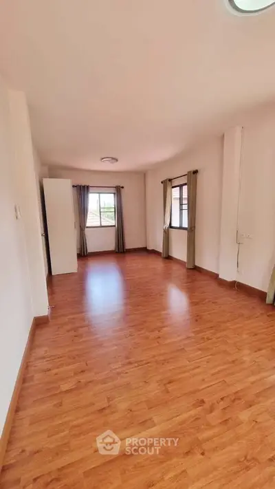 Spacious empty room with wooden flooring and large windows, perfect for customization.